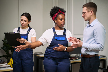Young adult Caucasian man discussing cleaning tasks with young adult Black woman and young adult...