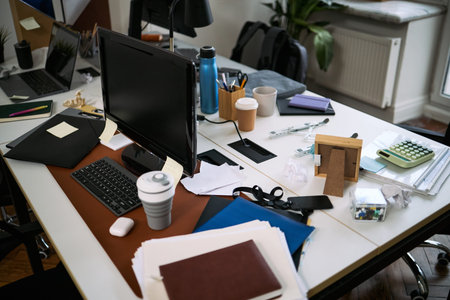 Messy office desk showing scattered documents, disposable coffee cups, reusable water bottle,...