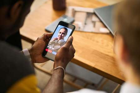 Over shoulder view of young adult man holding smartphone, browsing dating app profile beside male friend, suggesting online matchmaking, social connection, app marketing use