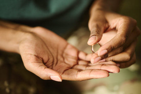 Hands of African American young holding wedding ring, contemplating divorce or separation. Concept of relationship breakdown, suitable for legal or counseling services, close up