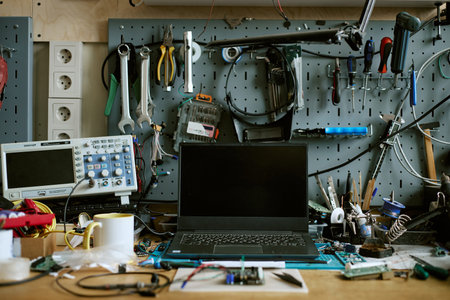 Laptop computer placed on electronics repair workbench with oscilloscope and tools. Suitable for hardware engineering, technology development and electronics maintenance marketing
