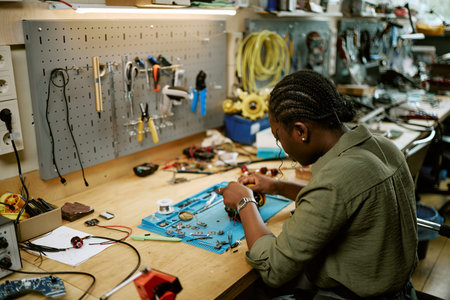 African American young woman assembling electronic components in workshop. Useful for STEM education campaigns, engineering training programs, and technology innovation promotions