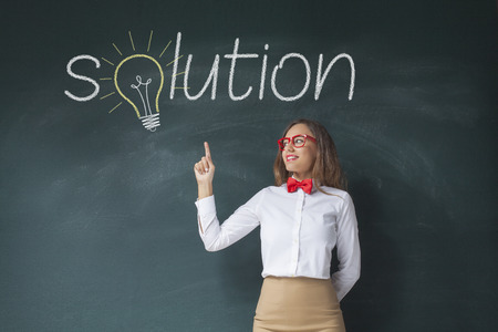 Businesswoman standing against solution text chalk drawing on blackboard and pointing on itの写真素材