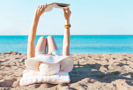 Portrait of a young brunette relaxing on the beach, reading a bookの写真素材