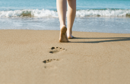 Young girl walking on sandy beach leaving footprints in the sandの写真素材