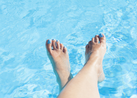 Woman's feet against blue water of the poolの写真素材