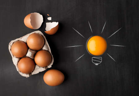 Egg yolk ball forming a shape of illuminated light bulb on blackboardの写真素材