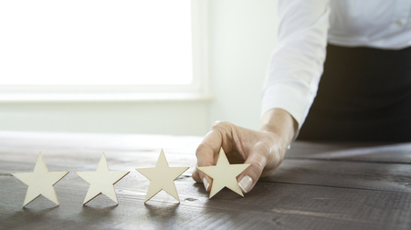 Businesswoman puts the fourth wooden star on a tableの写真素材