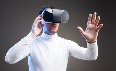 Young man wearing virtual reality device over grey background