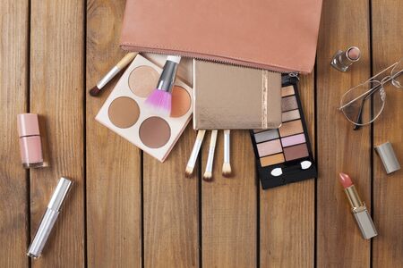Female beauty items on wooden background. Make up products, makeup purse, brushes, eyeshadowの写真素材