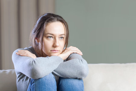 Young woman lying at home in living room sitting on sofa. She feeling sad and worried suffering...