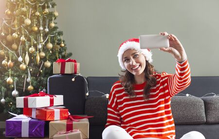 Happy young woman taking selfie over christmas treeの写真素材