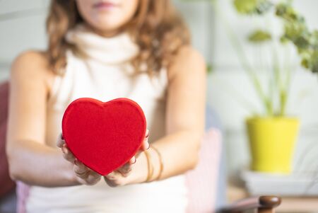 Woman holding heart shaped gift box at homeの写真素材