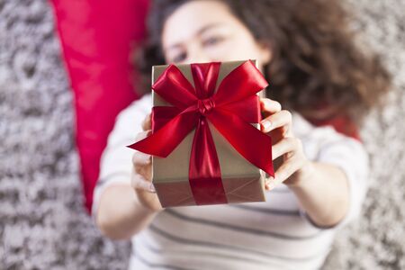 Happy pretty young woman holding gift box on carpetの写真素材