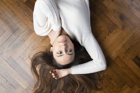 Unhappy young woman lying on wooden floor with arms above head
の写真素材