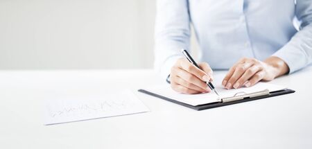 Woman's hands writing on sheet in a clipboard with a pen. Hands of businesswoman working with documents.の写真素材