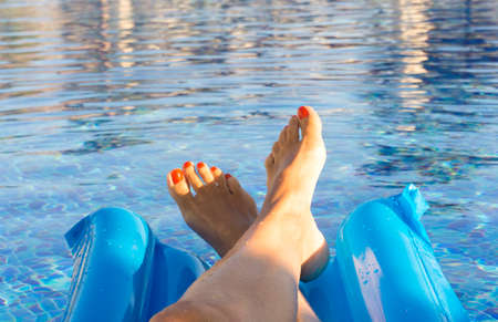 Woman's feet against blue water of the poolの写真素材