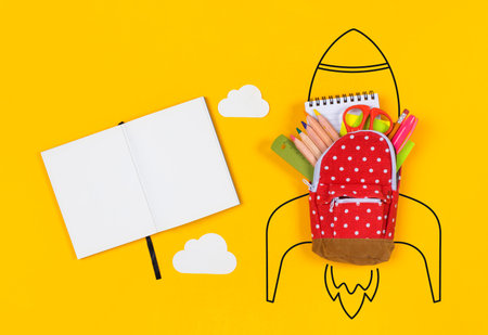 Back to school concept with miniature backpack, school supplies and rocket on yellow background.