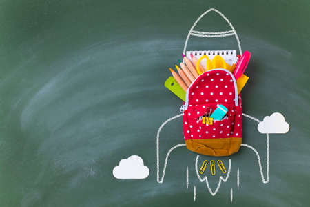 Back to school concept with miniature backpack, school supplies and rocket sketch over blackboard.の写真素材