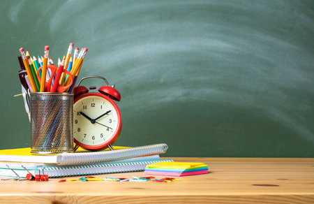 Pencil tray and alarm clock on notebook stack in classroom. Back to school conceptの写真素材