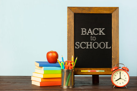 Blackboard with the text back to school written in it, an alarm clock, a pencil tray and a red apple...