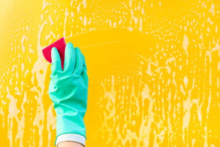 Female hand in green gloves cleaning window pane with rag. Cleaning concept