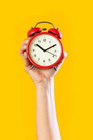 Woman's hand on a yellow background isolated with an alarm clock