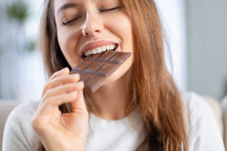 Cheerful young woman eating chocolate at homeの写真素材