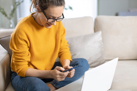 Young woman using mobile phone while sitting a sofa at home