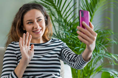 Young smiling woman video chatting using mobile phone at homeの写真素材