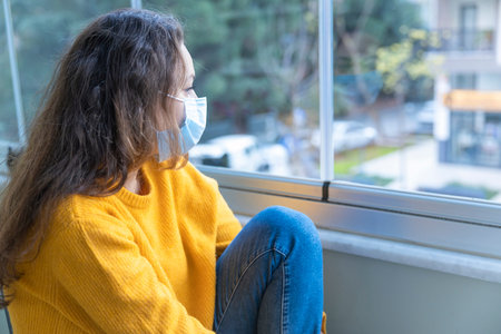 Young woman in medical mask staying at home under quarantine