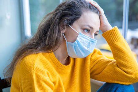 Young woman in medical mask staying at home under quarantineの写真素材
