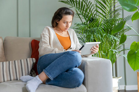 Young woman sitting on sofa in living room and using tablet pc