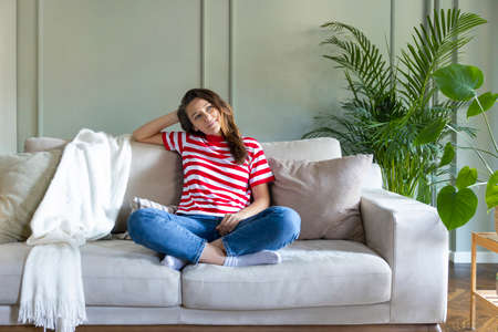 Young woman looking thoughtful while relaxing on the sofa at homeの写真素材