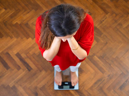 Sad young woman standing on scale. She is not satisfied with the result. Diet and healthy living concept.の写真素材