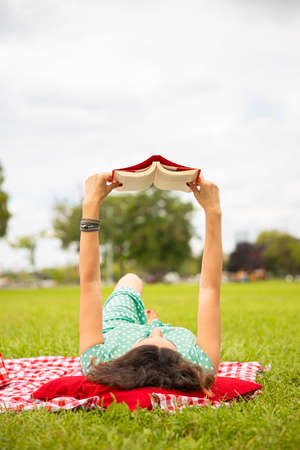 Young woman wearing green dress reading a book while relaxing in the parkの写真素材