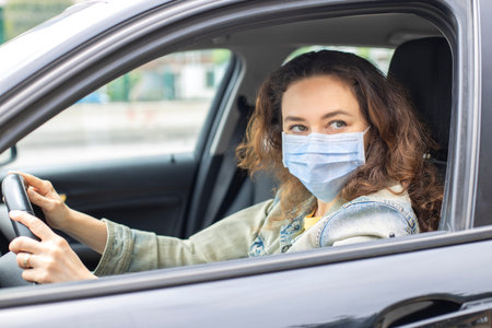 Young woman in a mask sitting in a car, protective mask against , driver on a city street during a...