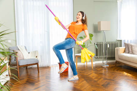 Full length cheerful young housewife using broom dancing having fun in living roomの写真素材