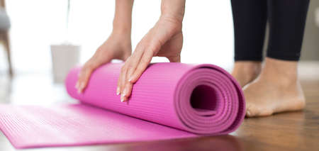 Young woman rolling her yoga mat after exercising and doing meditation at homeの写真素材