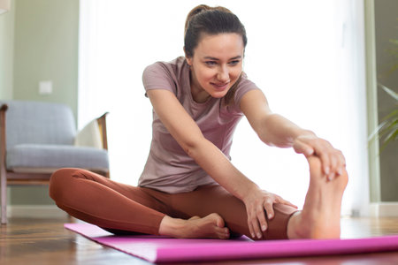 Beautiful sporty woman in sportswear doing stretching while sitting on the floor in living room