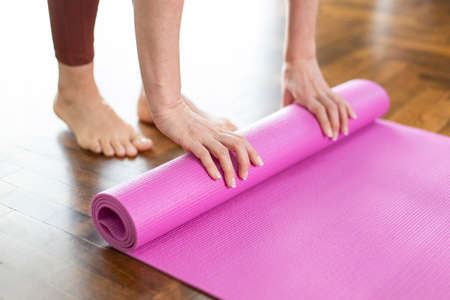 Young woman rolling her yoga mat after exercising and doing meditation at homeの写真素材