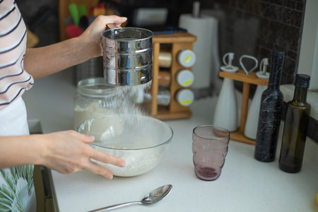 Woman sprinkling flour on dough in the kitchenの写真素材