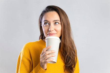 Smiling young woman drinking coffee from a paper cup on white backgroundの写真素材