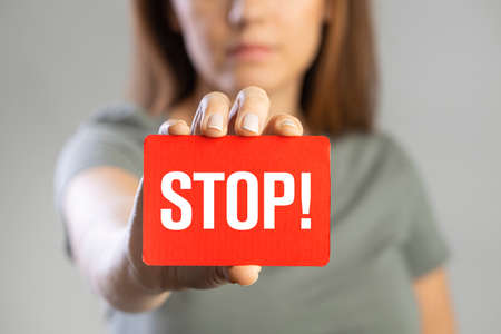 Young woman holding red stop card on gray backgroundの写真素材