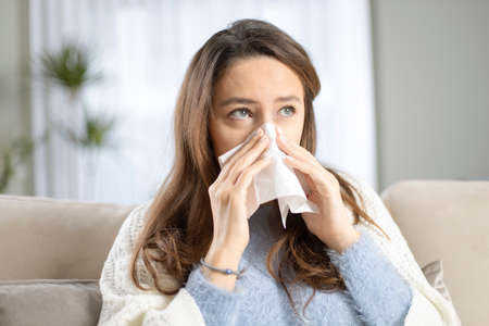 Sick woman blowing her nose, she covered with blanketの写真素材