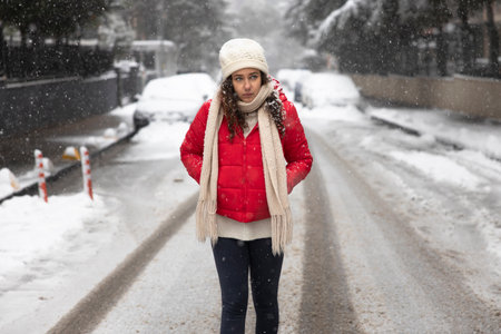Young woman in red coat walking in the city on a snowy winter dayの写真素材