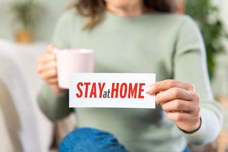 Closeup of woman showing the message stay at home written in a paper. Stop the spreadingの写真素材