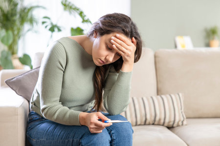Woman with flu virus measuring her temperature with a thermometer and touching her forehead