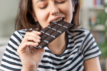 Young woman eating chocolate bar in living room