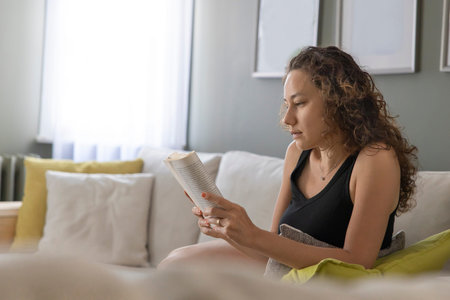 Young woman lying on sofa and reading a book